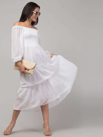 Women in white printed fit & flare dress with off-shoulder design, holding a clutch.