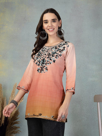 Woman wearing peach embroidered rayon kurti with three-quarter sleeves and floral embroidery on the neckline, paired with black pants.