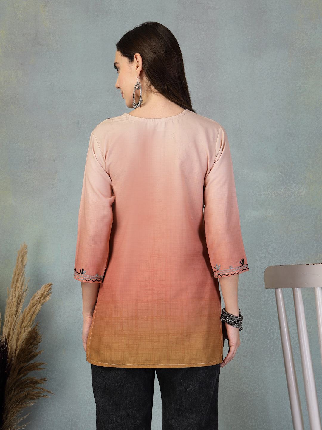 Back view of a woman wearing a peach embroidered rayon kurti with three-quarter sleeves and black pants against a gray background.