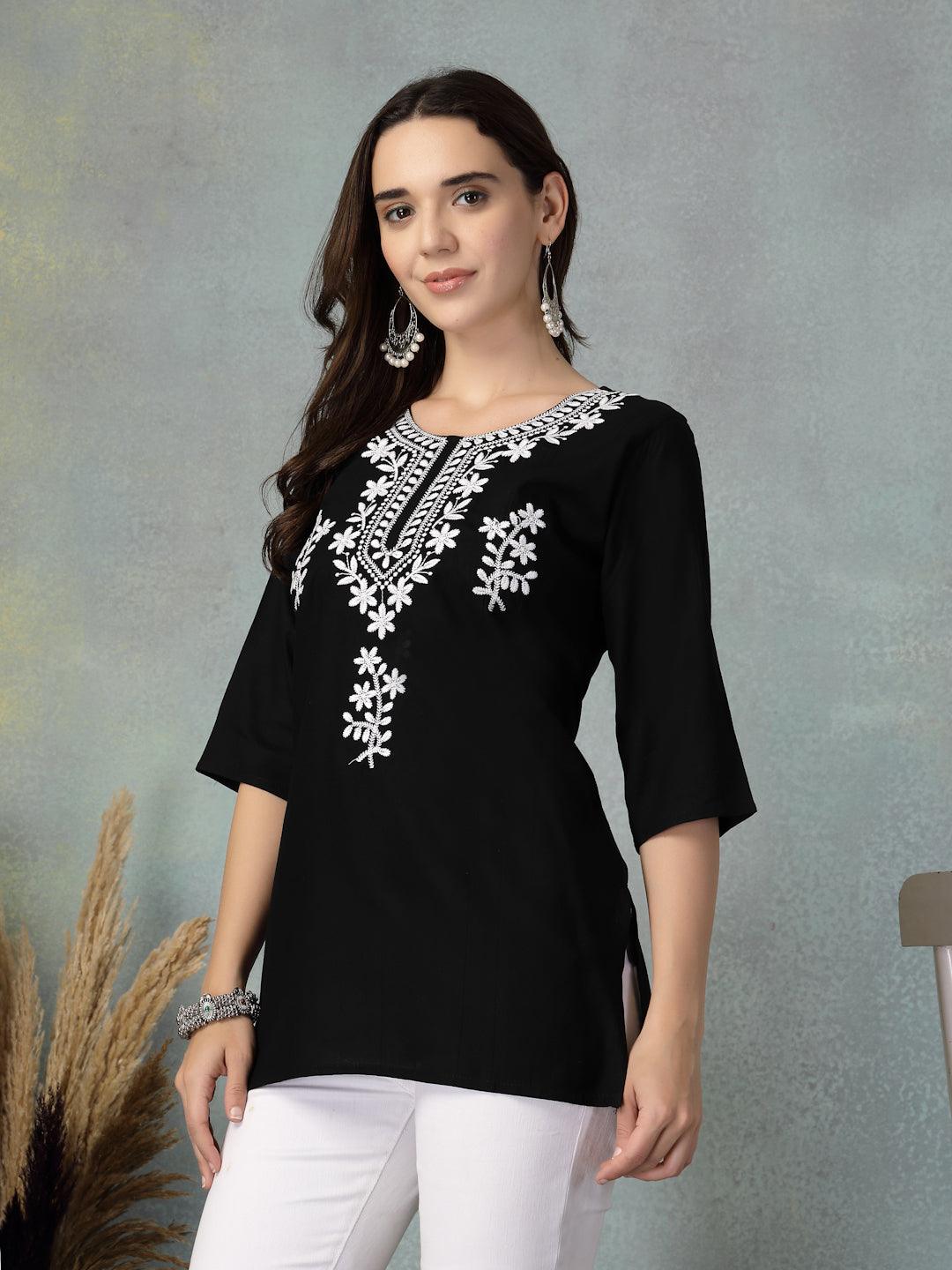Woman wearing black embroidered rayon kurti with white floral designs paired with white pants against a grey backdrop