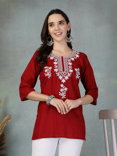 Woman wearing maroon embroidered rayon kurti with white floral designs, paired with white pants and silver jewelry