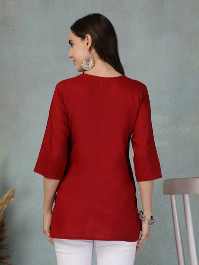 Back view of maroon embroidered rayon kurti worn with white bottoms against a gray textured wall background
