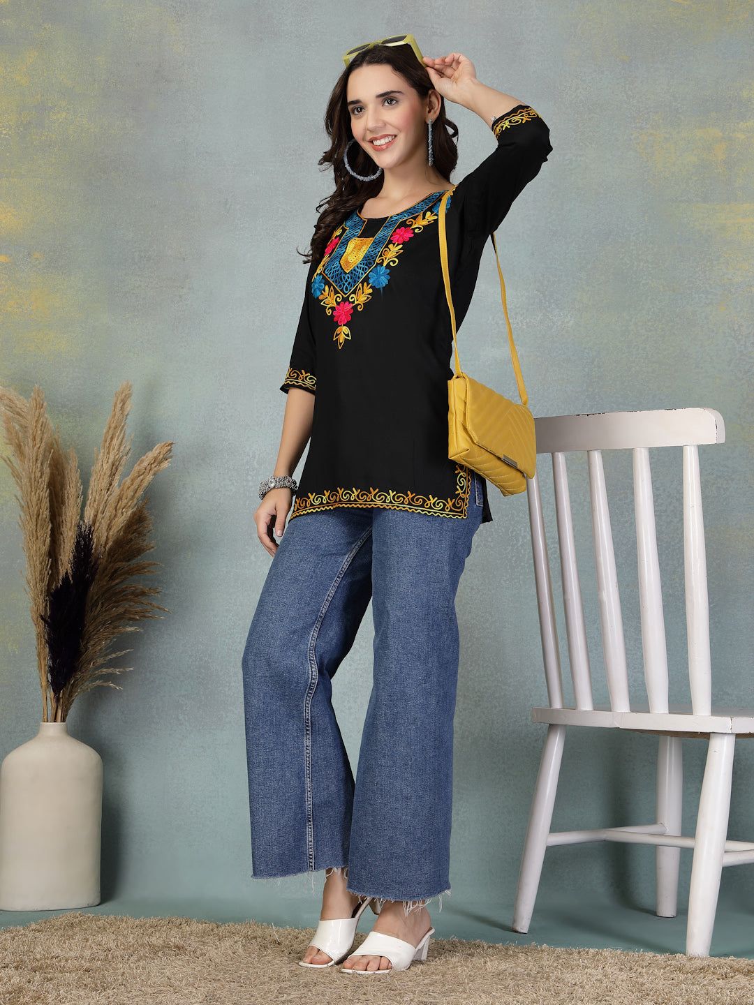 Woman wearing black embroidered rayon kurti paired with blue jeans and white heels, accessorized with a yellow handbag.