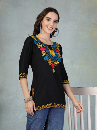 Black embroidered rayon kurti with colorful floral embroidery, worn with jeans, featuring three-quarter sleeves and intricate detailing.