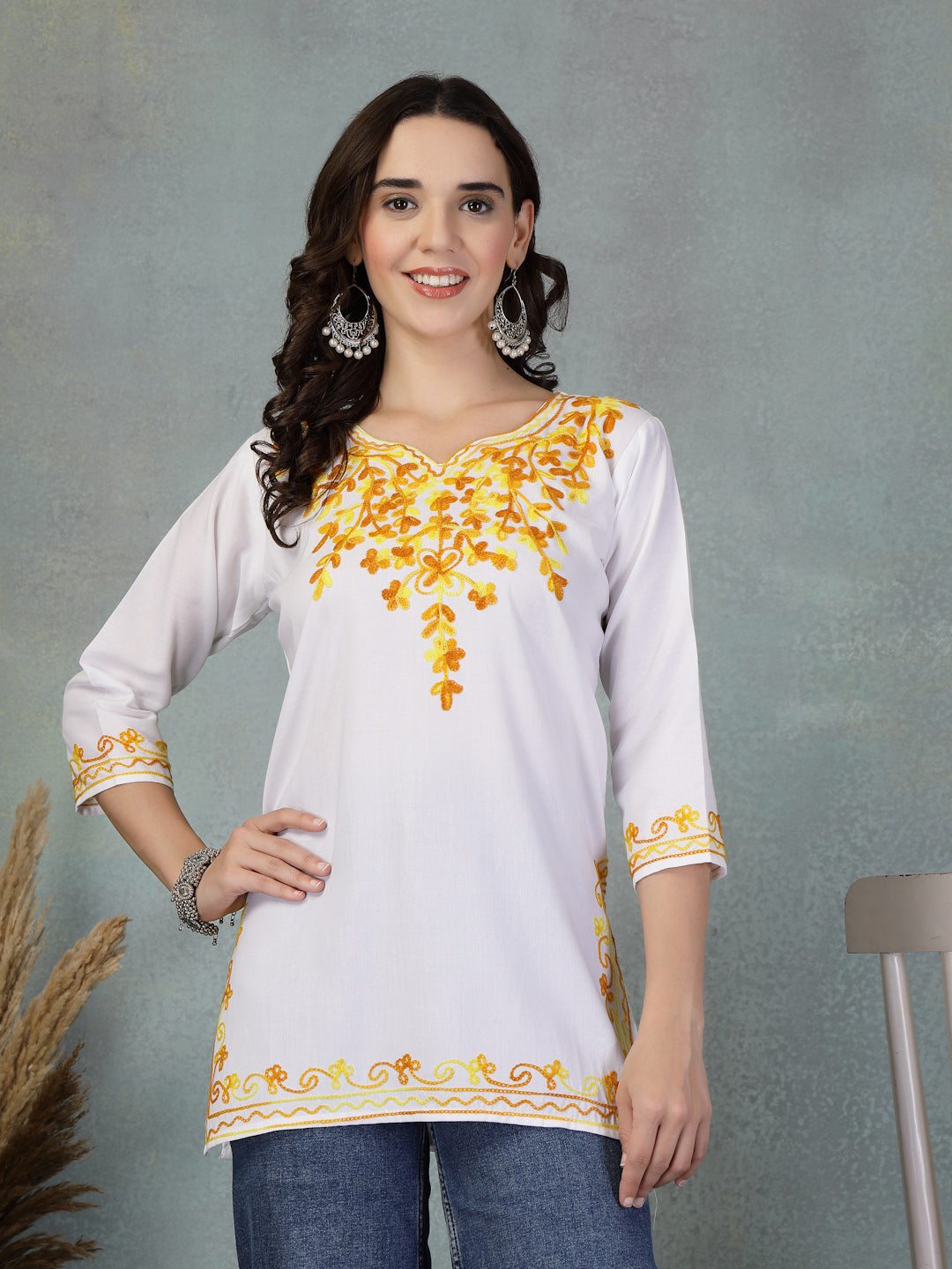 White embroidered rayon kurti with yellow floral embroidery on neckline, sleeves, and hem, styled with jeans.