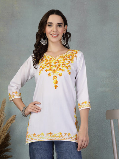 White embroidered rayon kurti with yellow floral embroidery on neckline, sleeves, and hem, styled with jeans.
